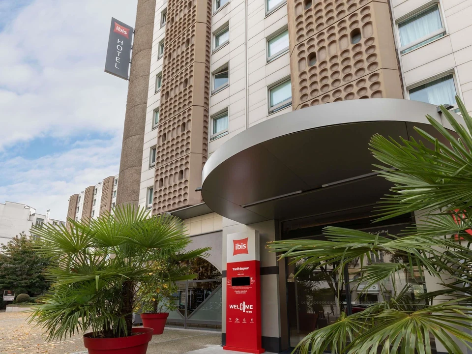 Entrance to ibis Paris Tour Eiffel Cambronne with red hotel signs and palm plants.