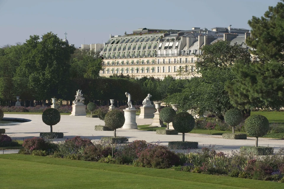 Le Meurice Paris seen across a formal garden with statues, flower beds and trees.