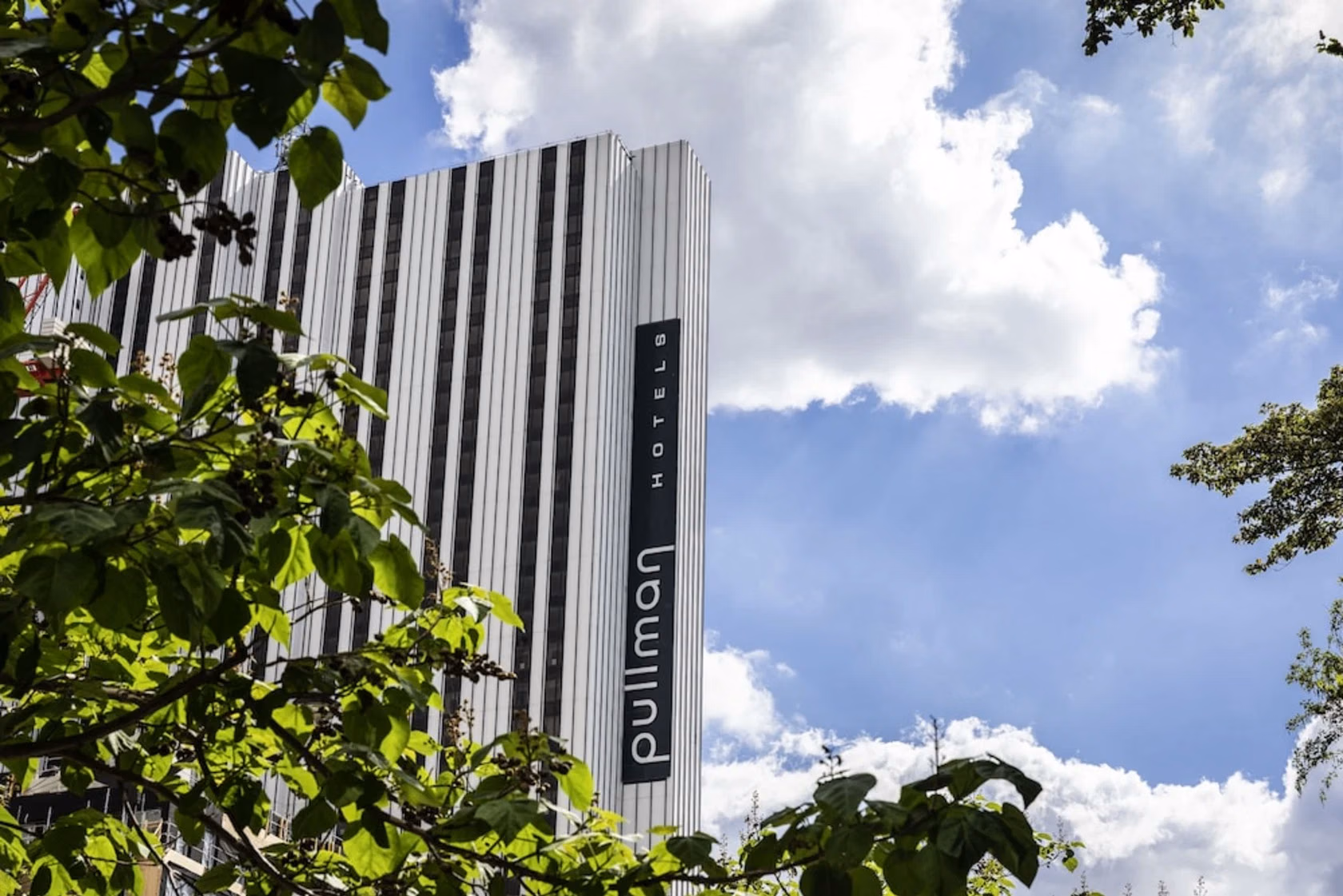 Hotel facade with a vertical Pullman sign and foliage in the foreground.